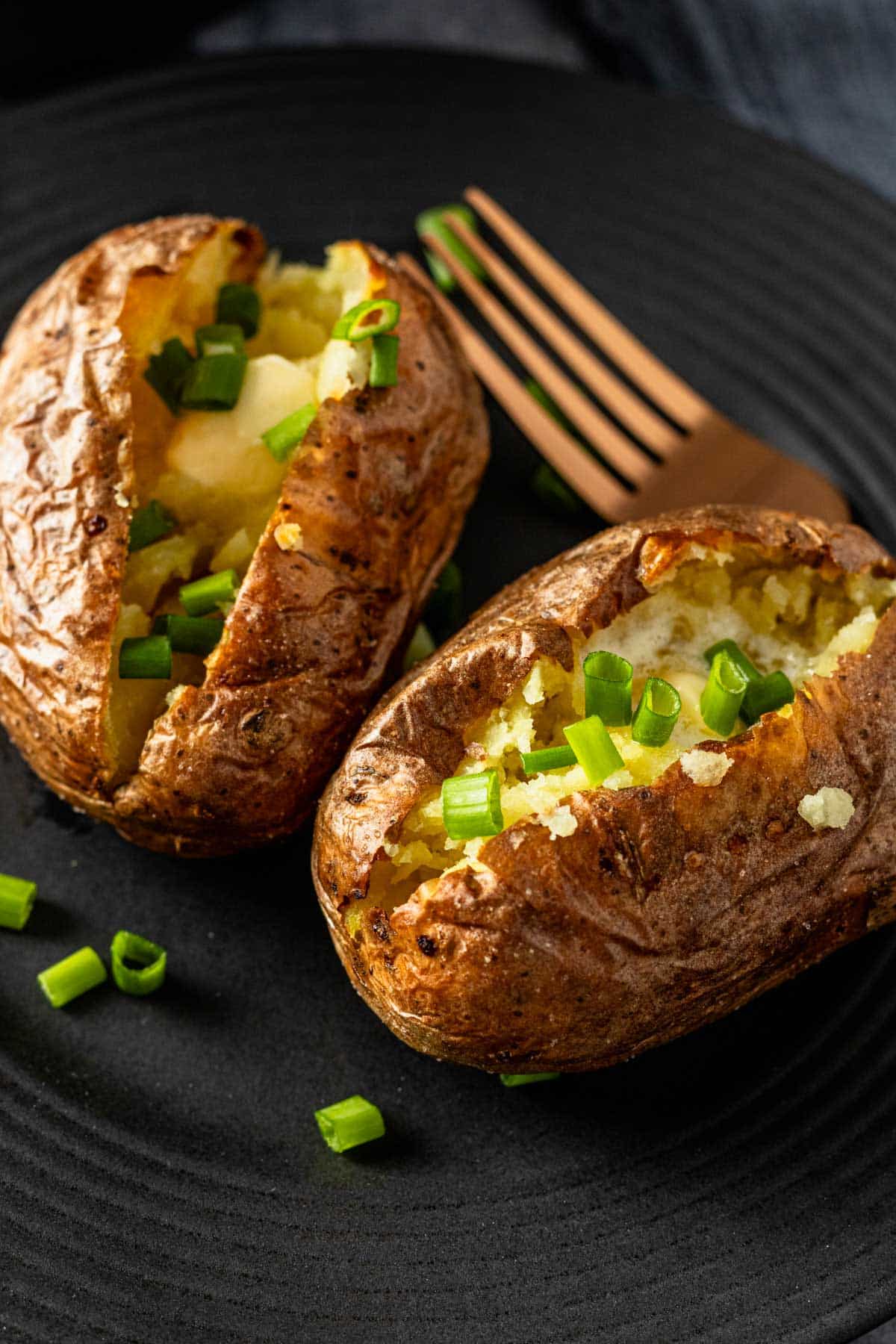 two air fryer baked potatoes cut in half topped with melting butter and chopped green onions.