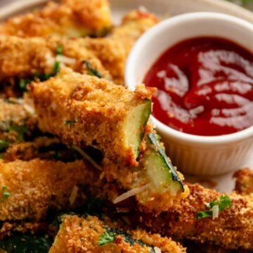 perfectly roasted golden brown zucchini fries served with red sauce.