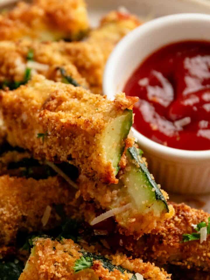 perfectly roasted golden brown zucchini fries served with red sauce.