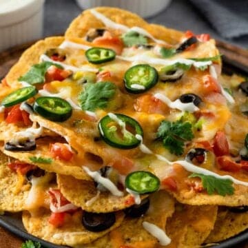 cheesy nachos with toppings on wooden board