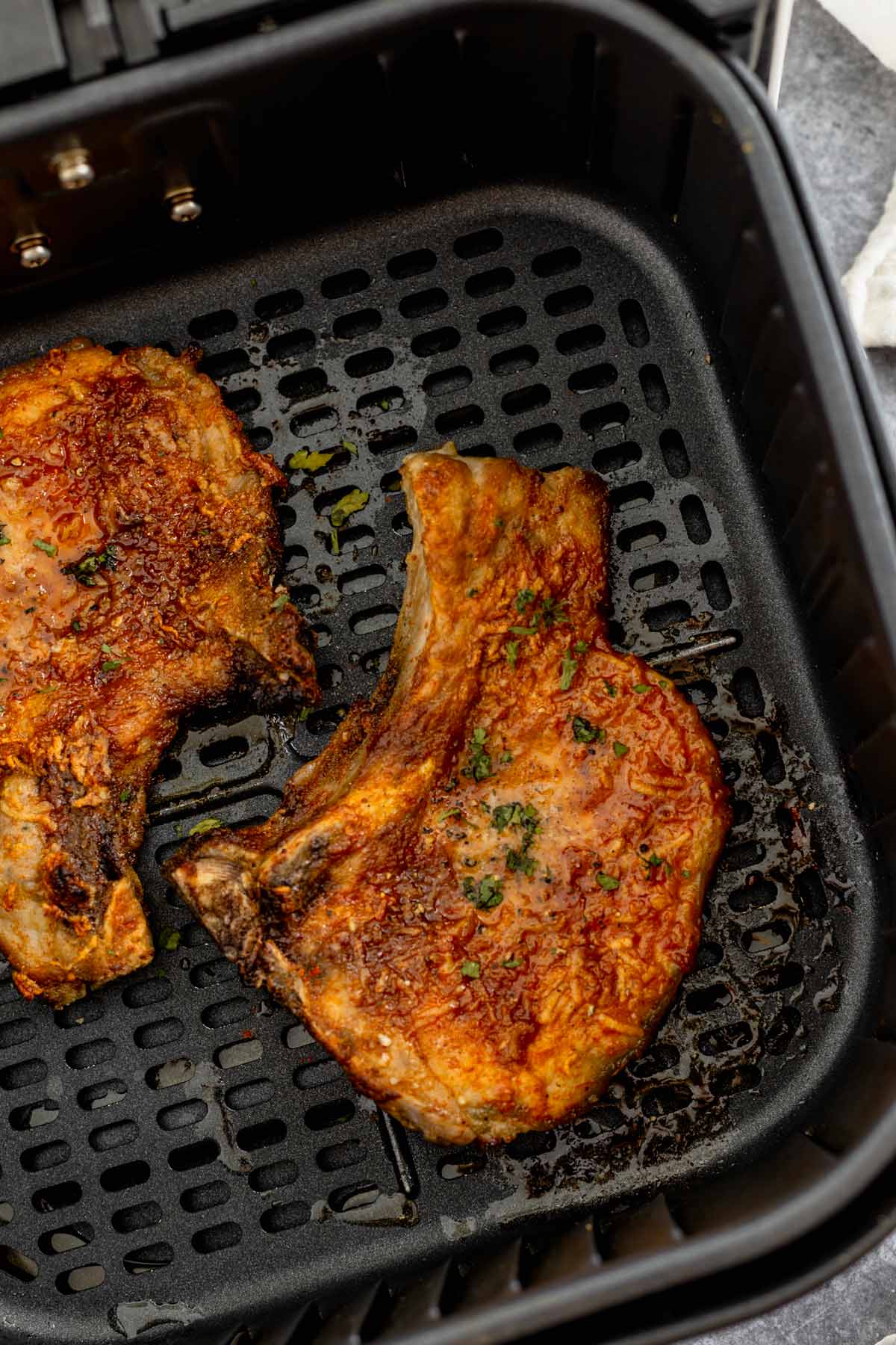 cooked air fryer pork chops in air fryer basket with butter on top
