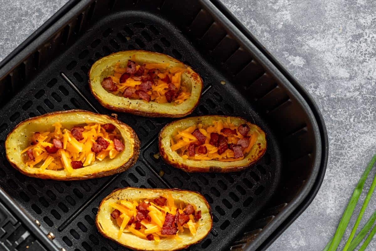 cooked potato skins with cheese and bacon in the air fryer basket.