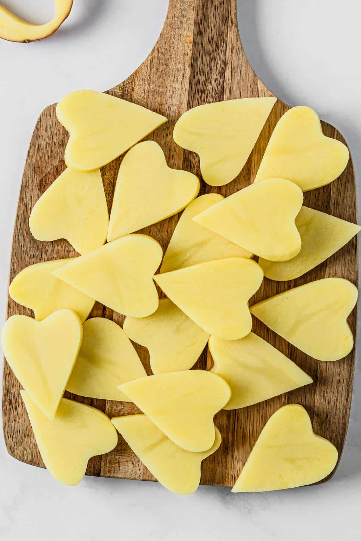 raw heart shaped potatoes on a wooden slicingboard