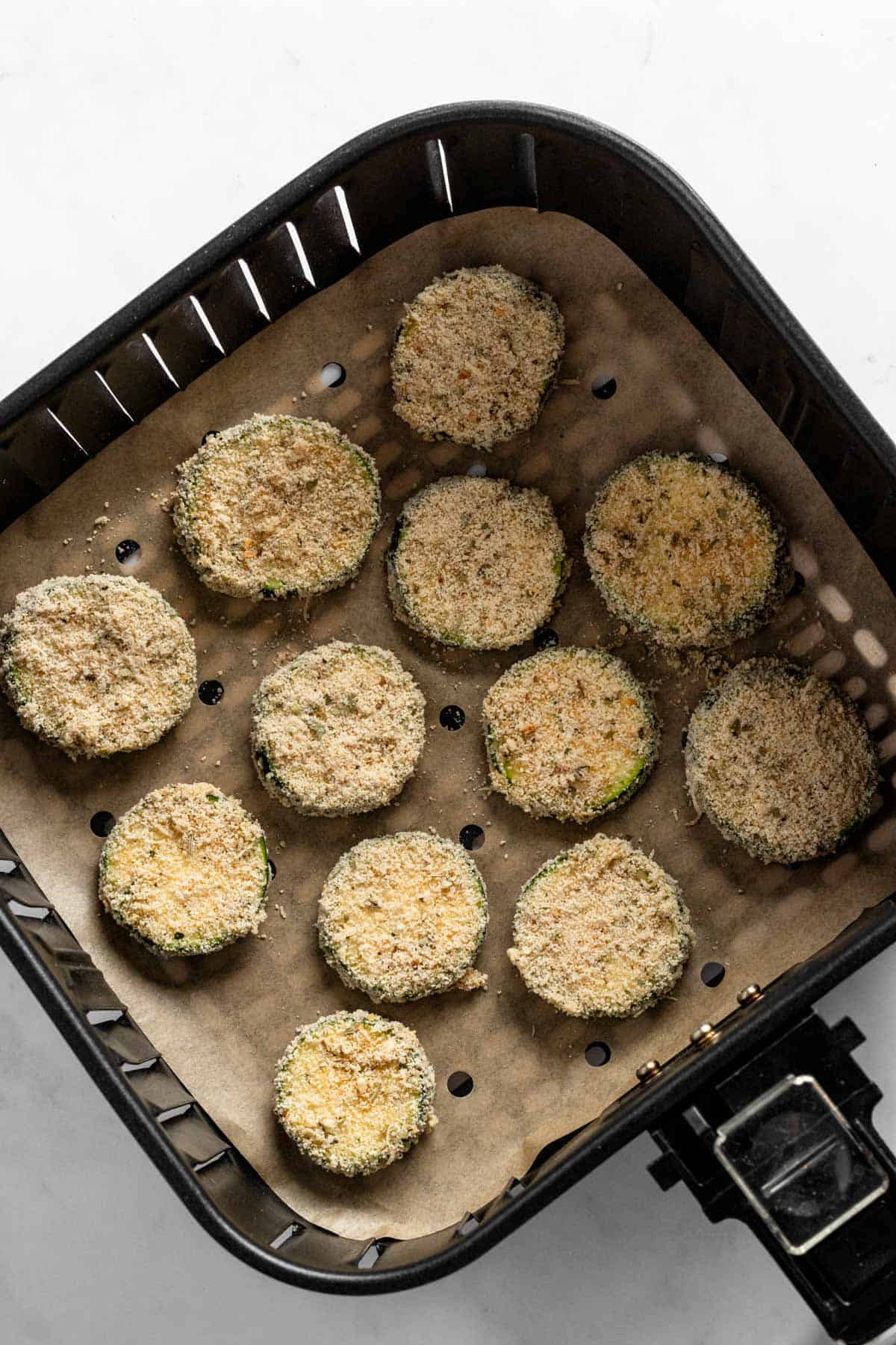 zucchini slices in parmesan and breadcrumb coating in a air fryer basket.