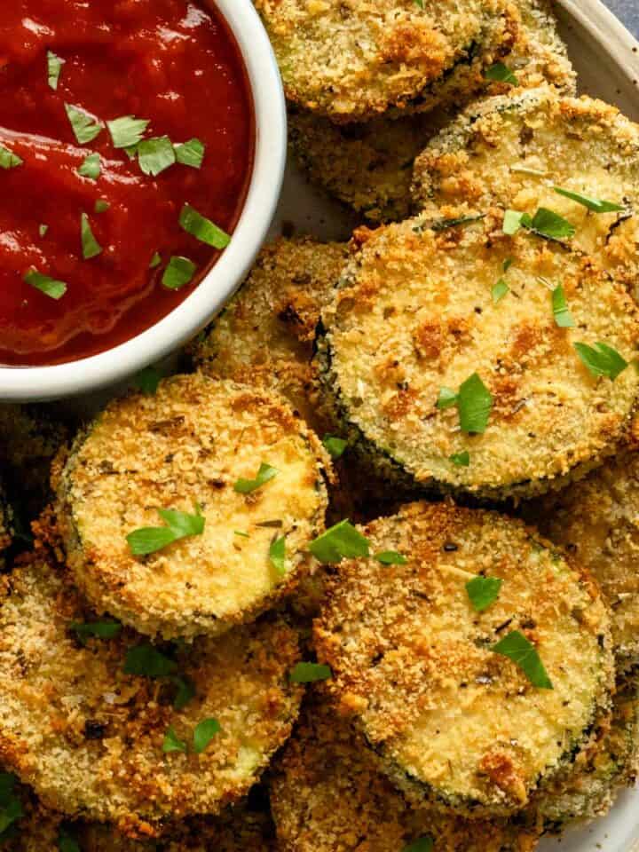 cooked air fryer zucchini slices on a bowl with red dipping sauce bowl.