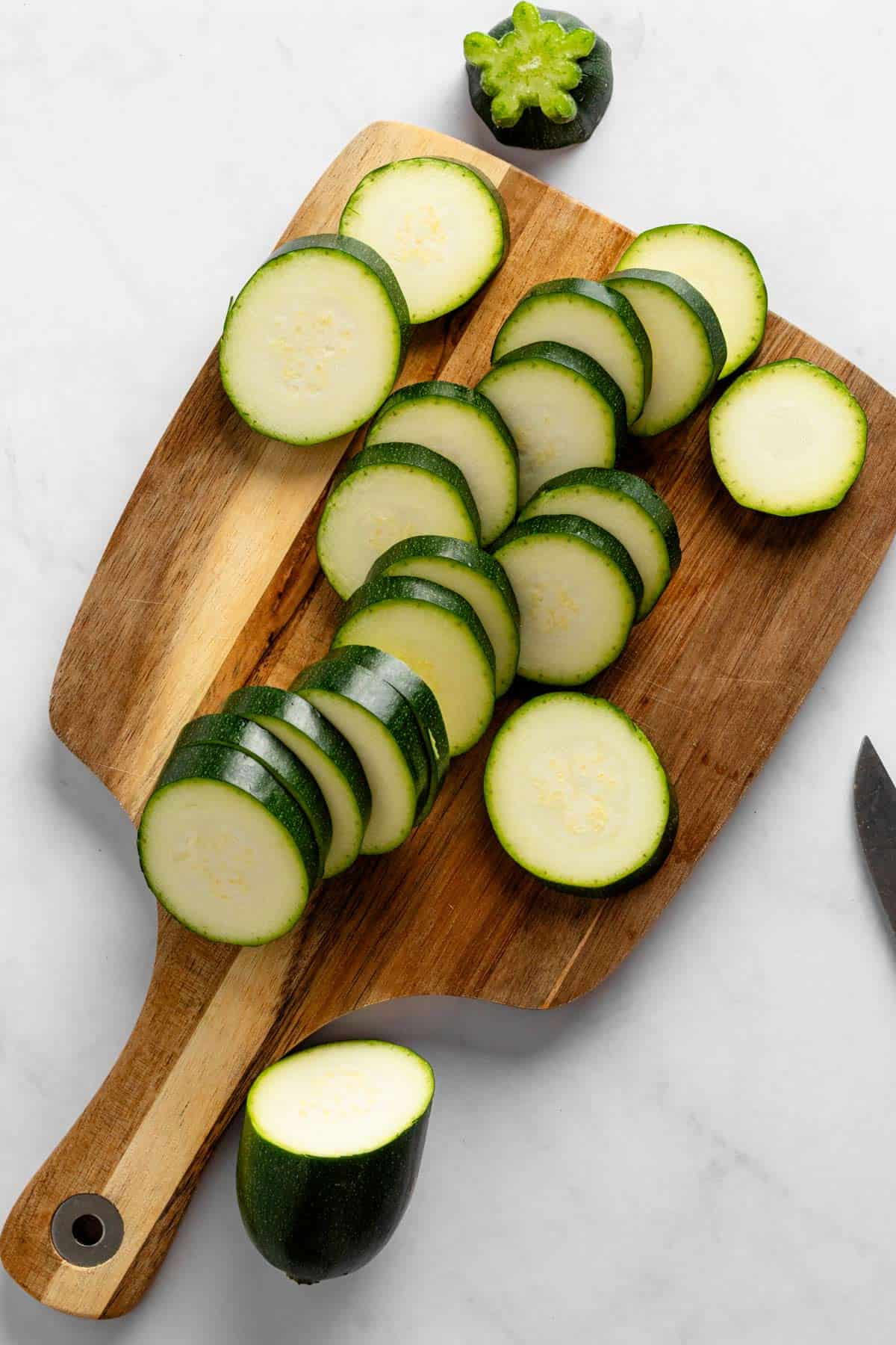 cutting zucchini into slices on wooden board.