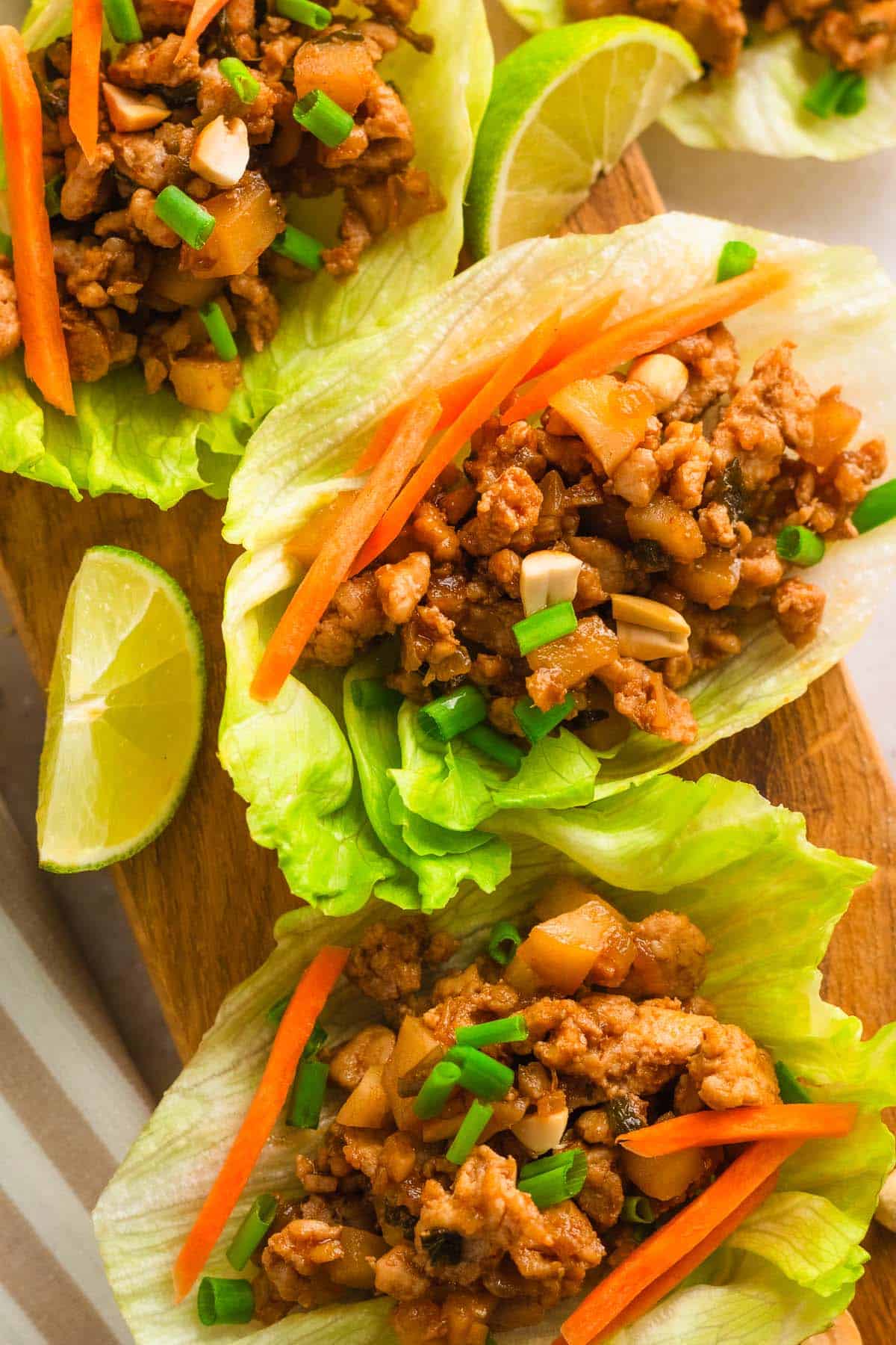 Chicken lettuce cups served with lime wedges on wooden board.