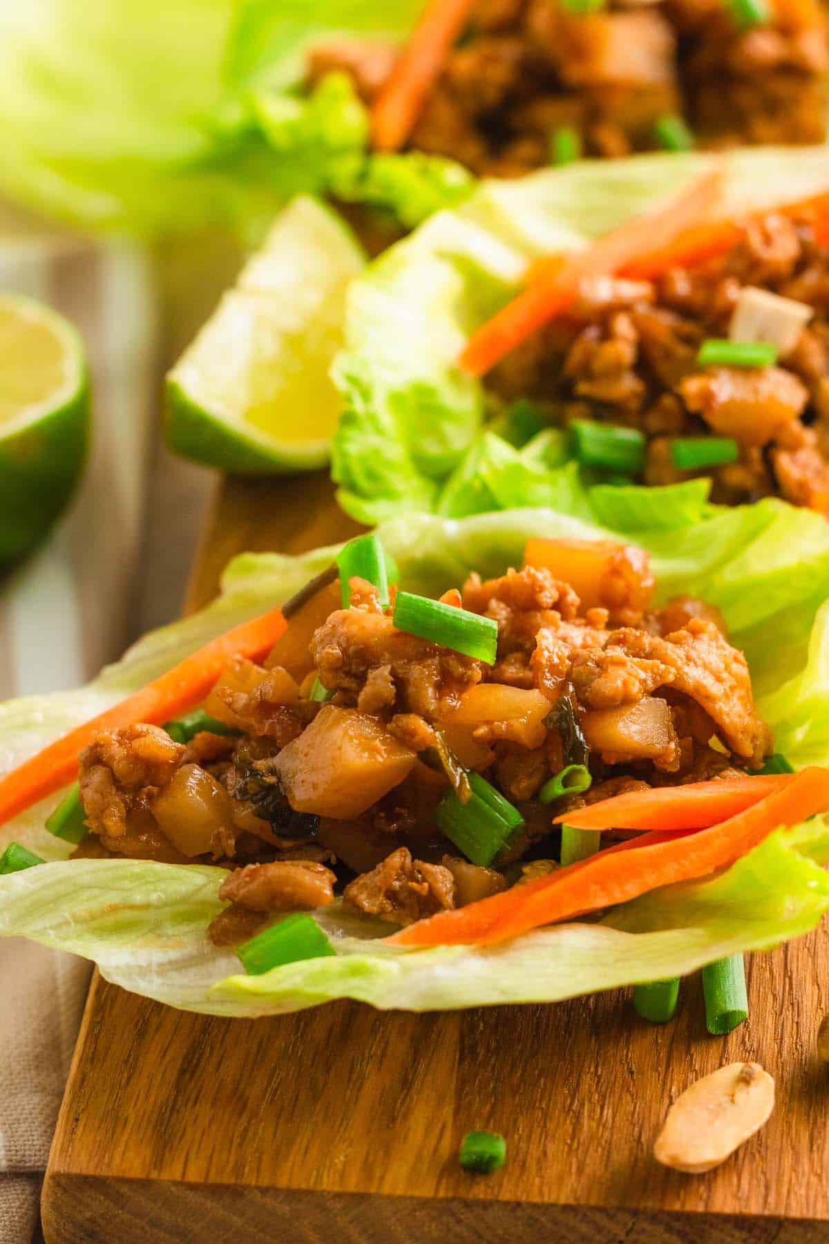 Close-up of chicken lettuce wraps topped with shredded carrots and scallions.