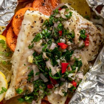 baked cod fillets in foil with chimichurri sauce, vegetables and lemon