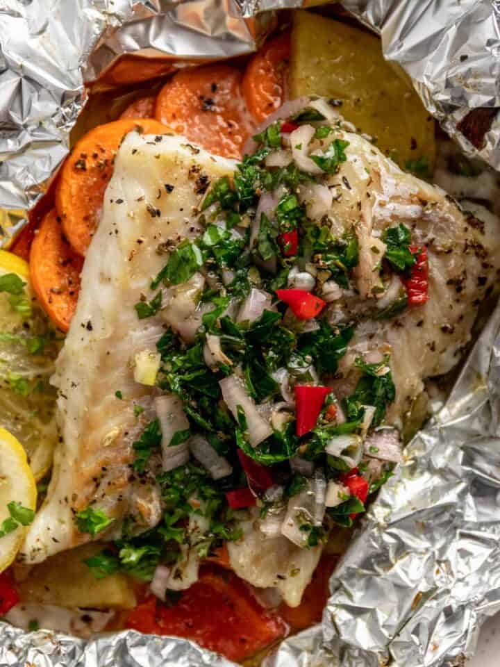 baked cod fillets in foil with chimichurri sauce, vegetables and lemon