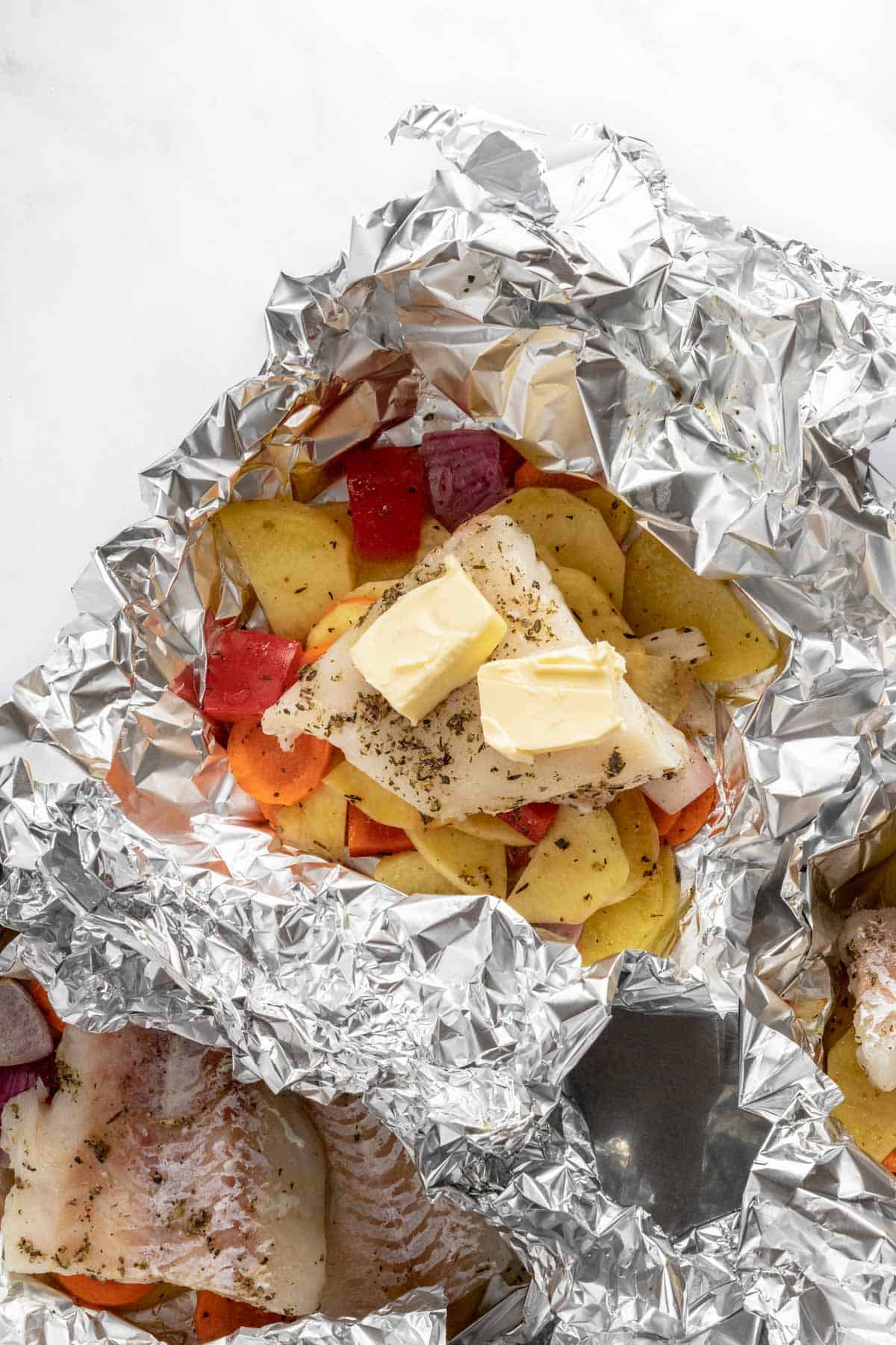 fish fillets and vegetables in foil topped with butter cubes before baking