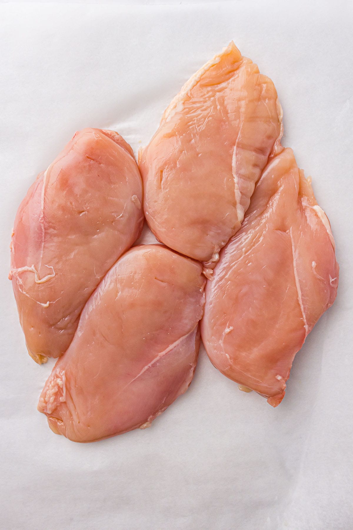 Raw boneless skinless chicken breasts on marble surface.