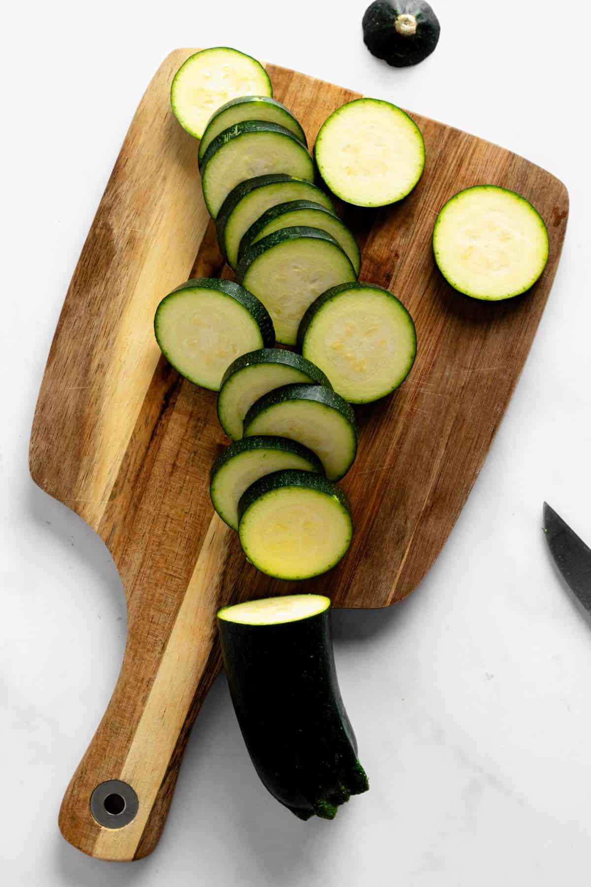 cutting zucchini into slices on wooden board.