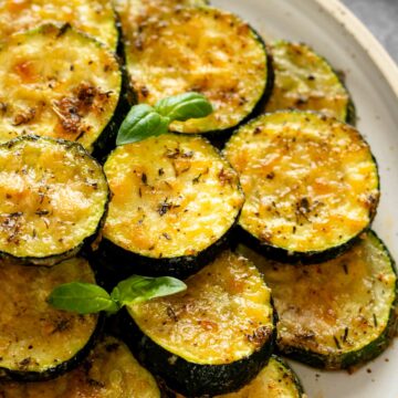 baked parmesan zucchini rounds garnished with fresh basil leaves.