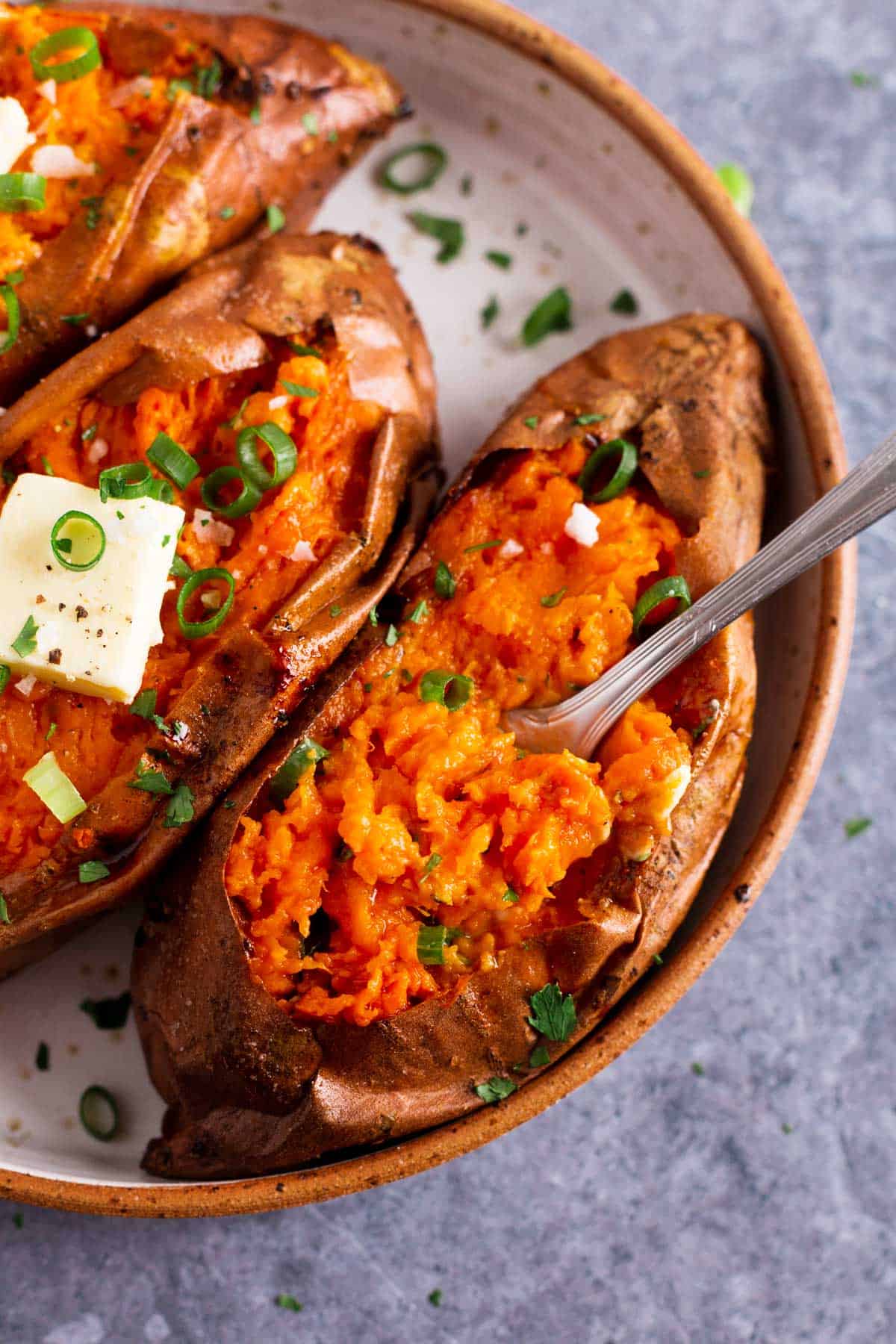 three baked sweet potatoes with butter and green onion