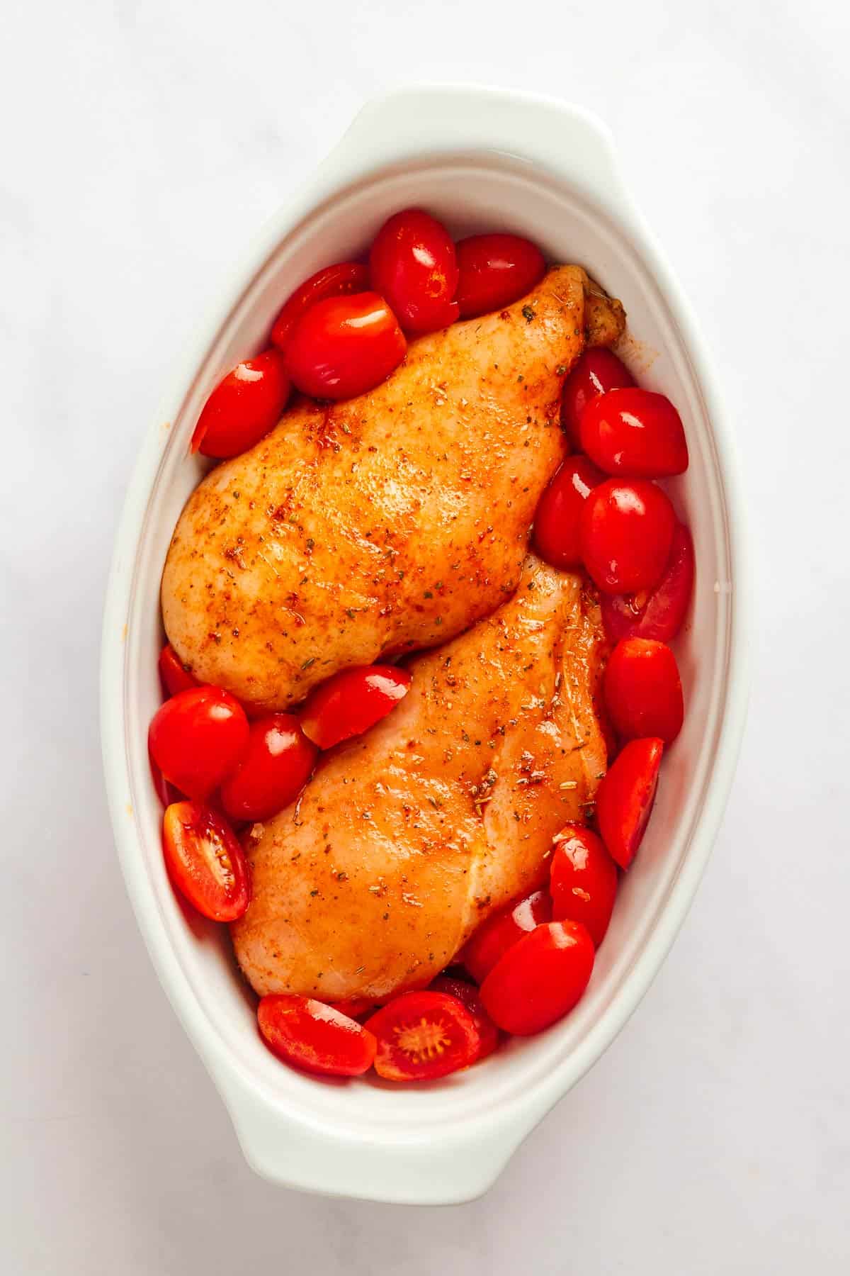 Chicken breasts coated in balsamic marinade with cherry tomatoes in baking dish.