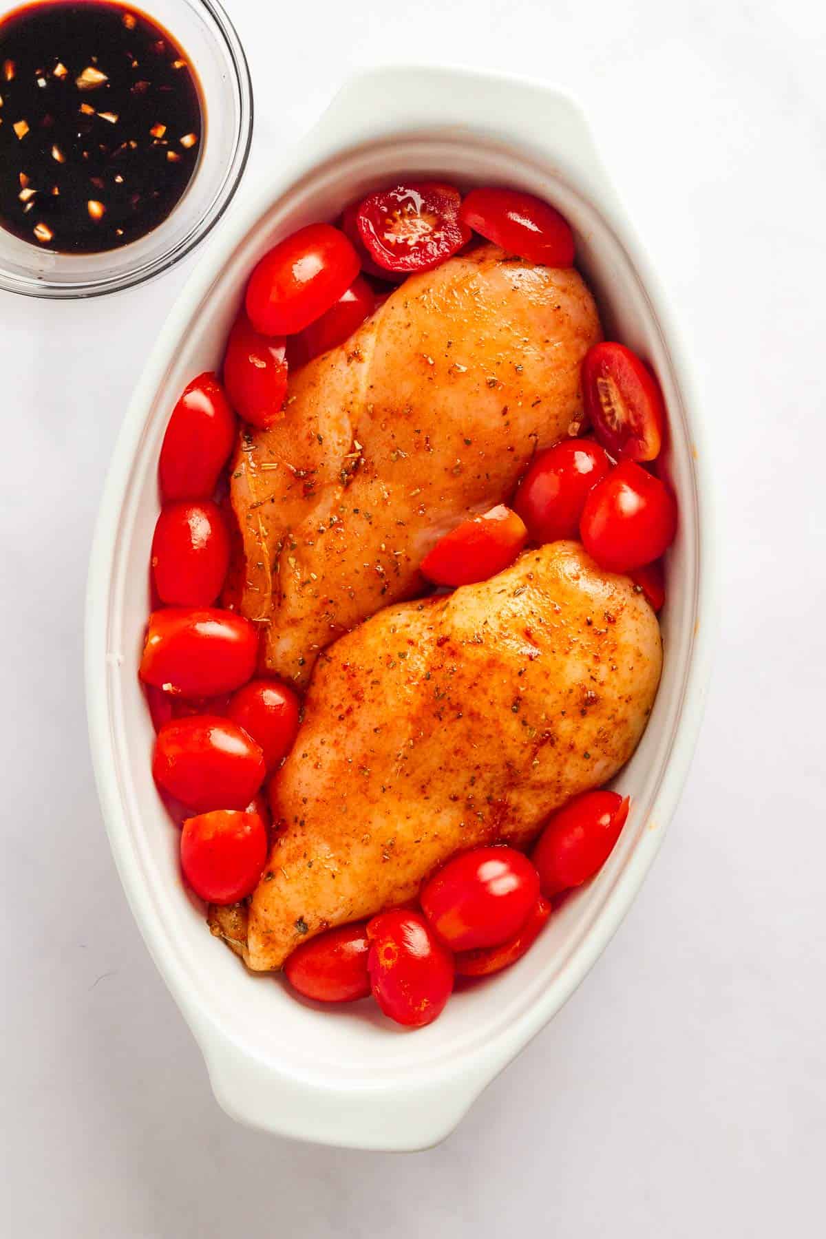 Chicken breasts coated in balsamic marinade with cherry tomatoes in baking dish.