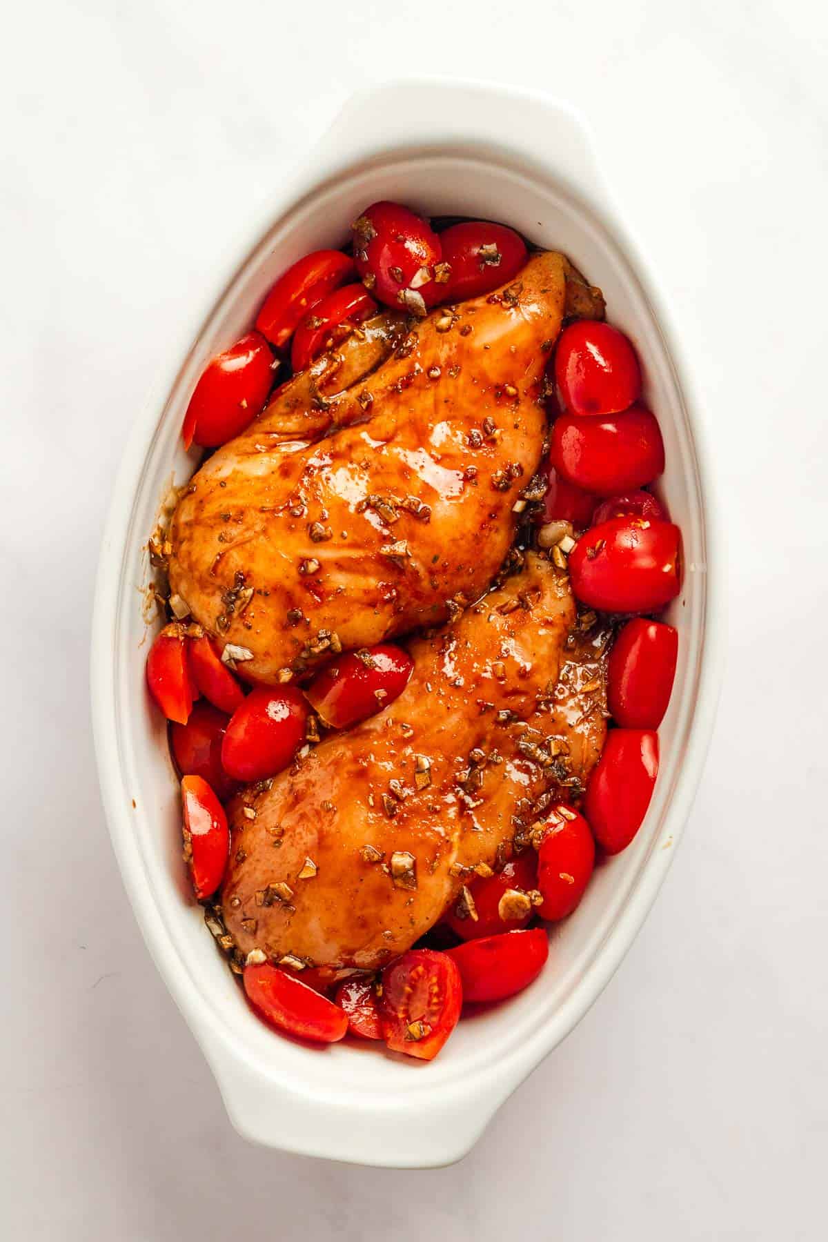 Chicken breast in baking dish with balsamic sauce and cherry tomatoes.