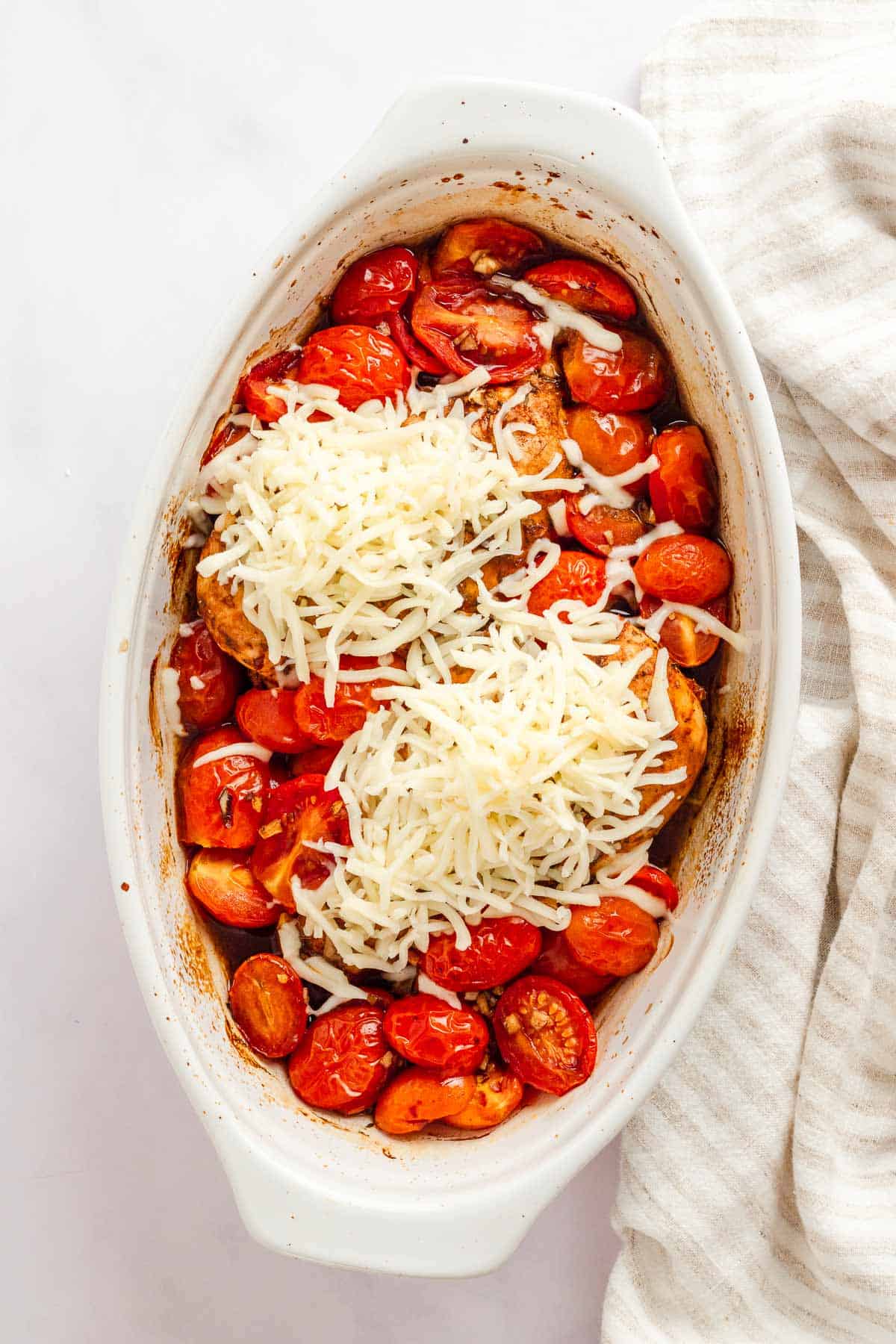 Chicken breast in baking dish with balsamic sauce and cherry tomatoes and cheese.