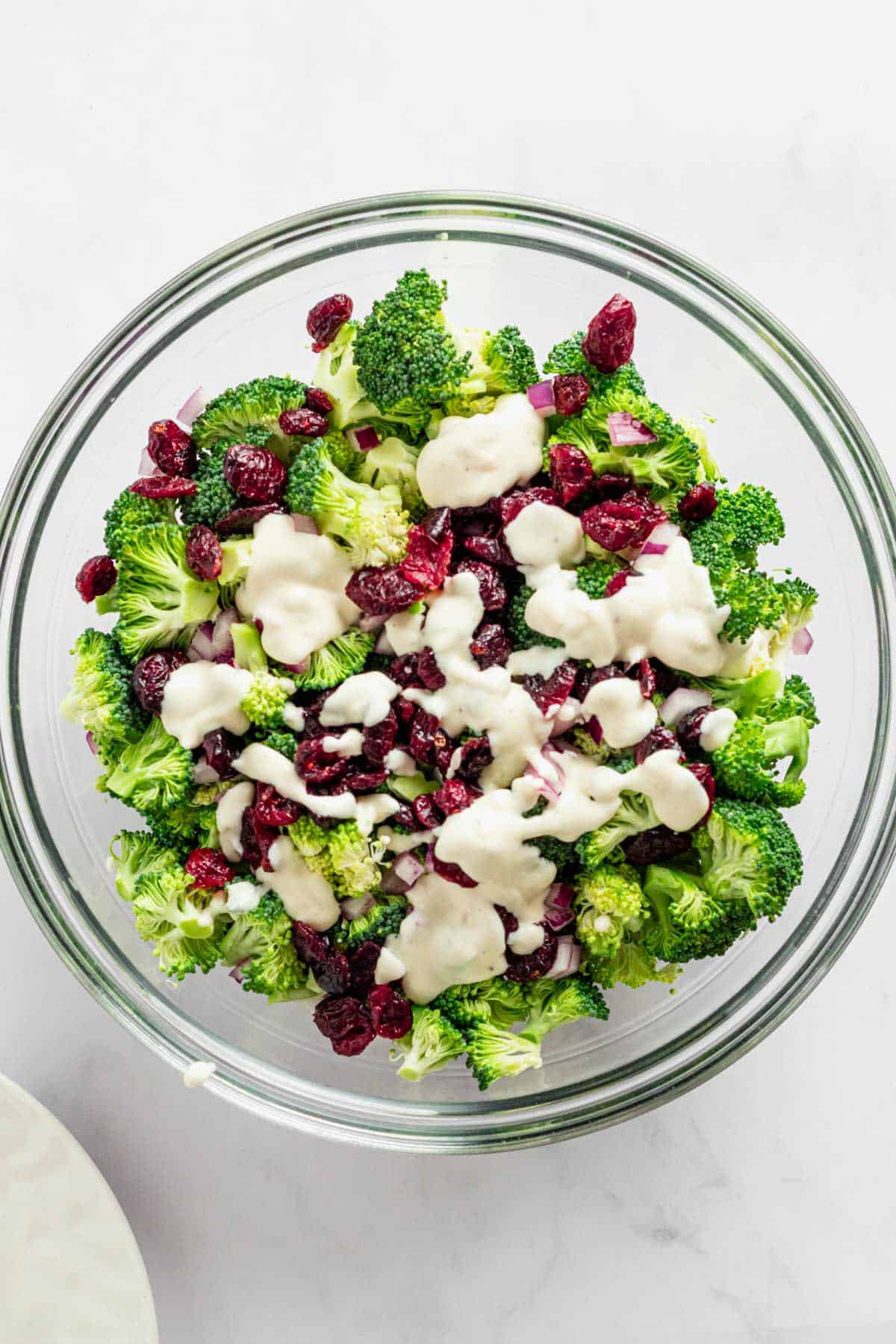 adding white dressing to broccoli salad bowl.