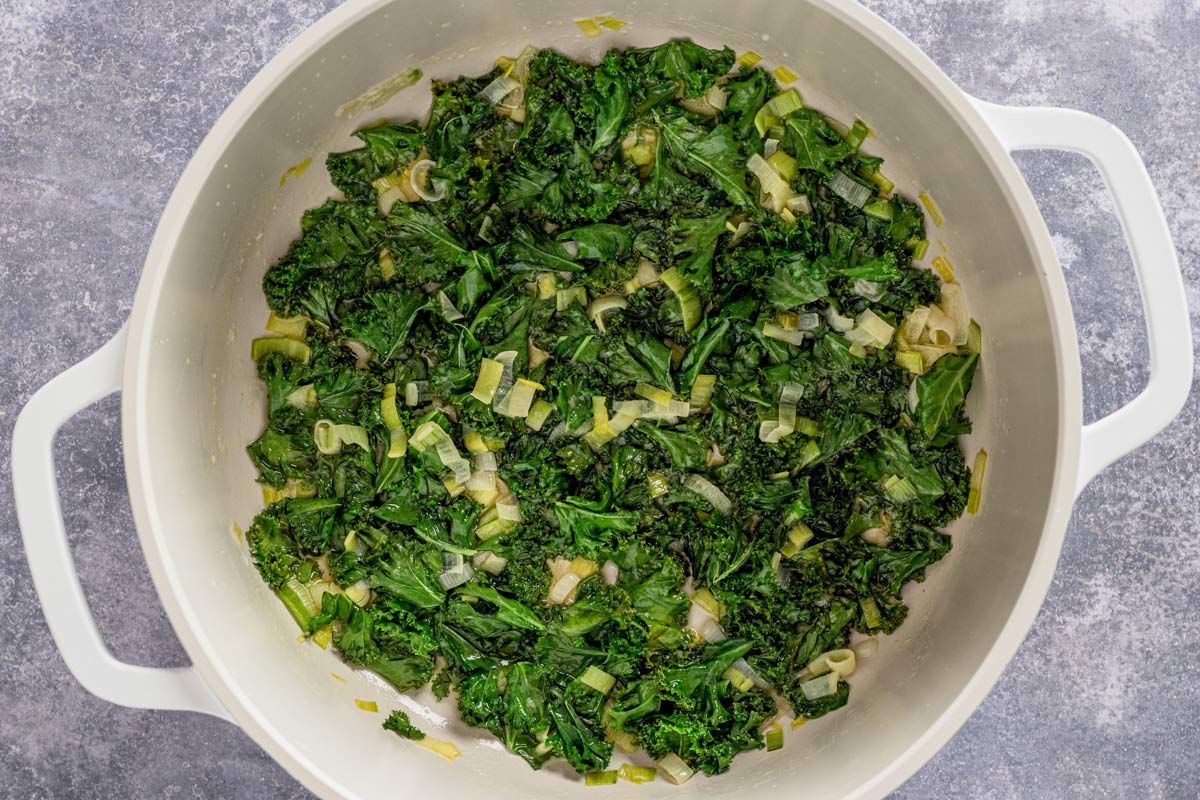 kale sauteing in a large white pot