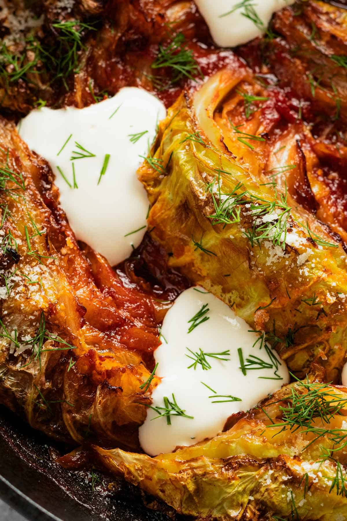caramelized cabbage wedges in skillet topped with sour cream and dill.