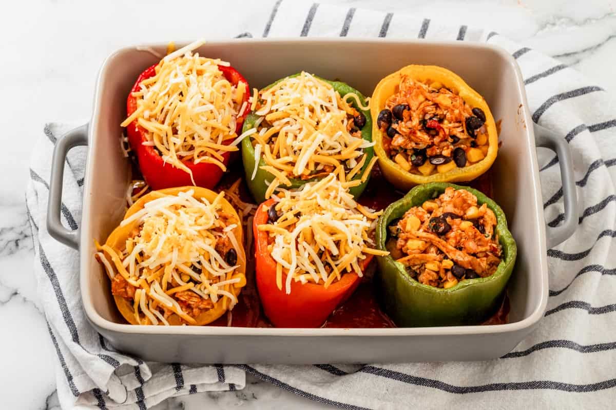 six bell peppers with chicken enchilada stuffing topped with cheese in baking dish