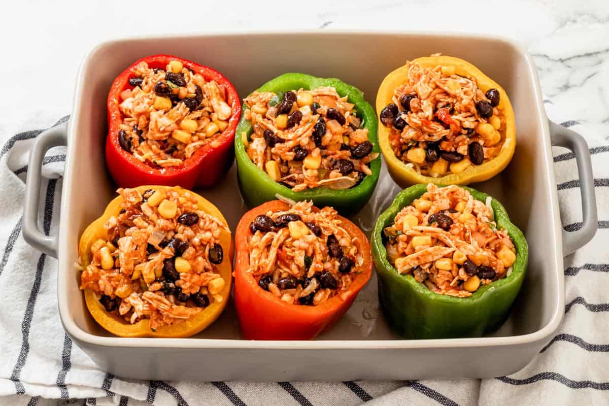 six bell peppers with chicken enchilada stuffing in baking dish