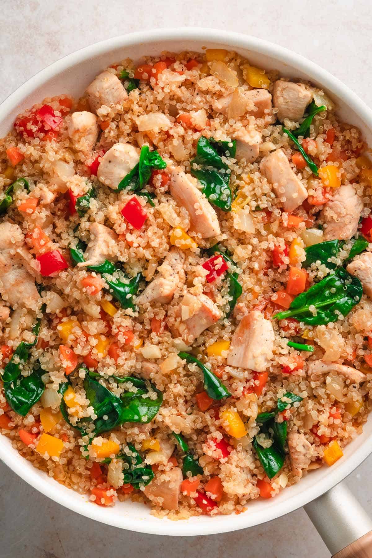 Quinoa and chicken mixture cooking in a pan with bright red and yellow peppers.