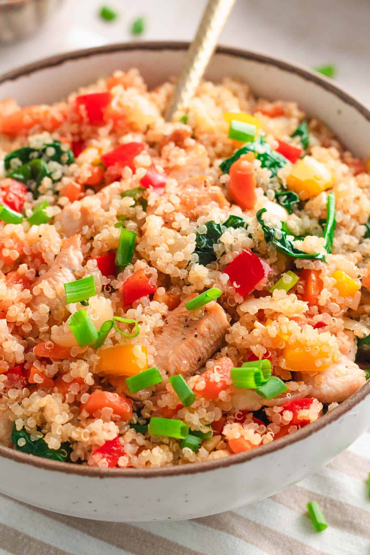 Chicken quinoa stir fry with bell peppers, spinach, and green onions in a skillet.