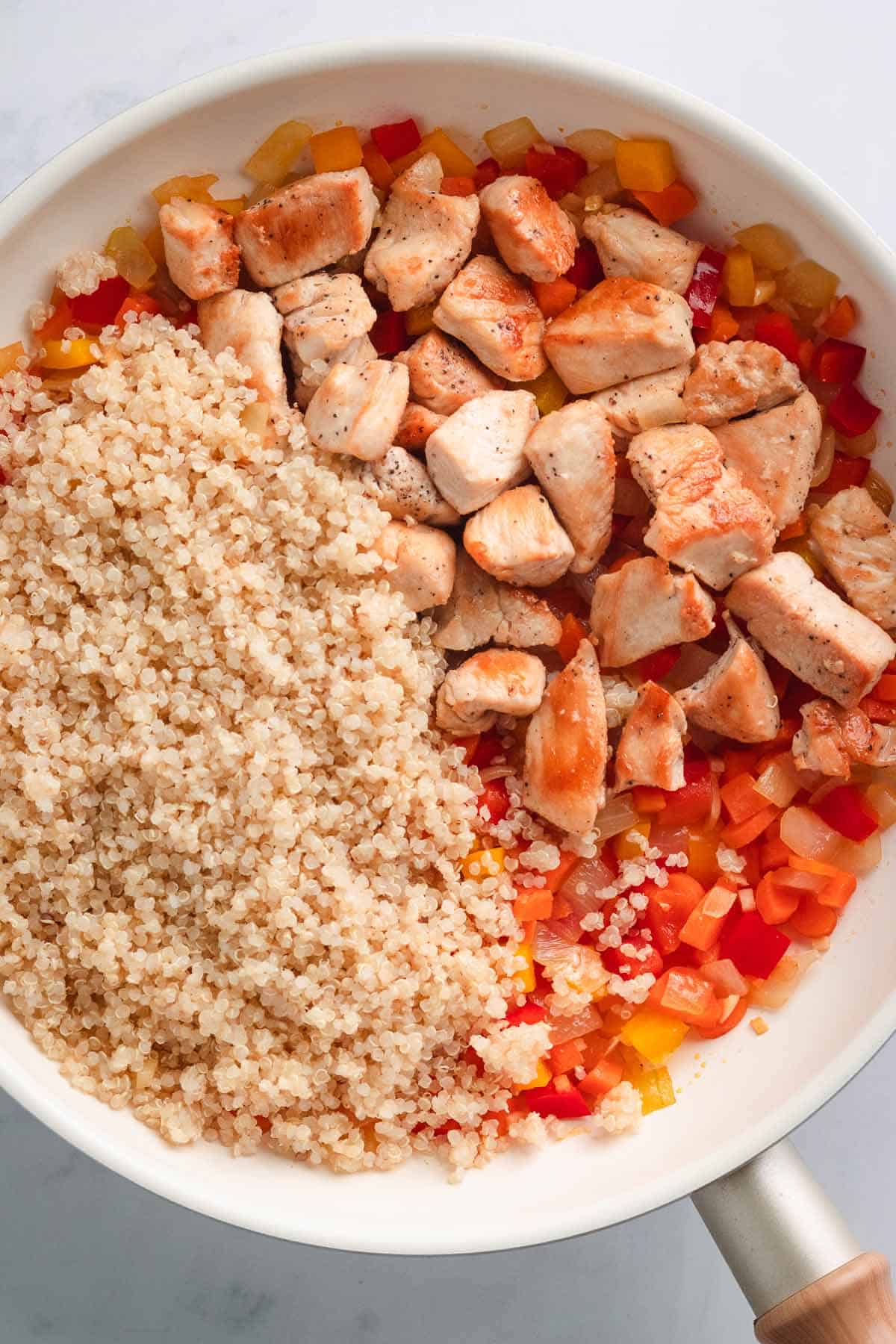 Cooked quinoa and diced chicken placed side by side in a skillet.