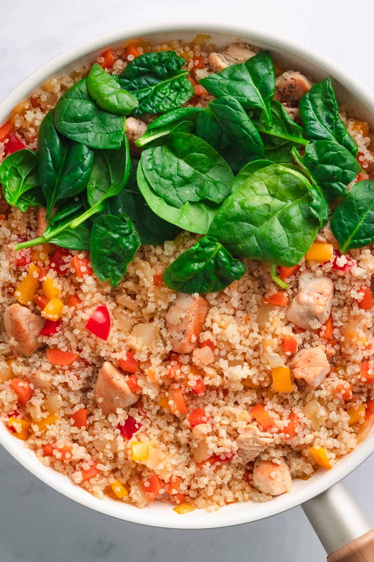 Fresh spinach leaves added on top of hot quinoa stir fry in skillet.