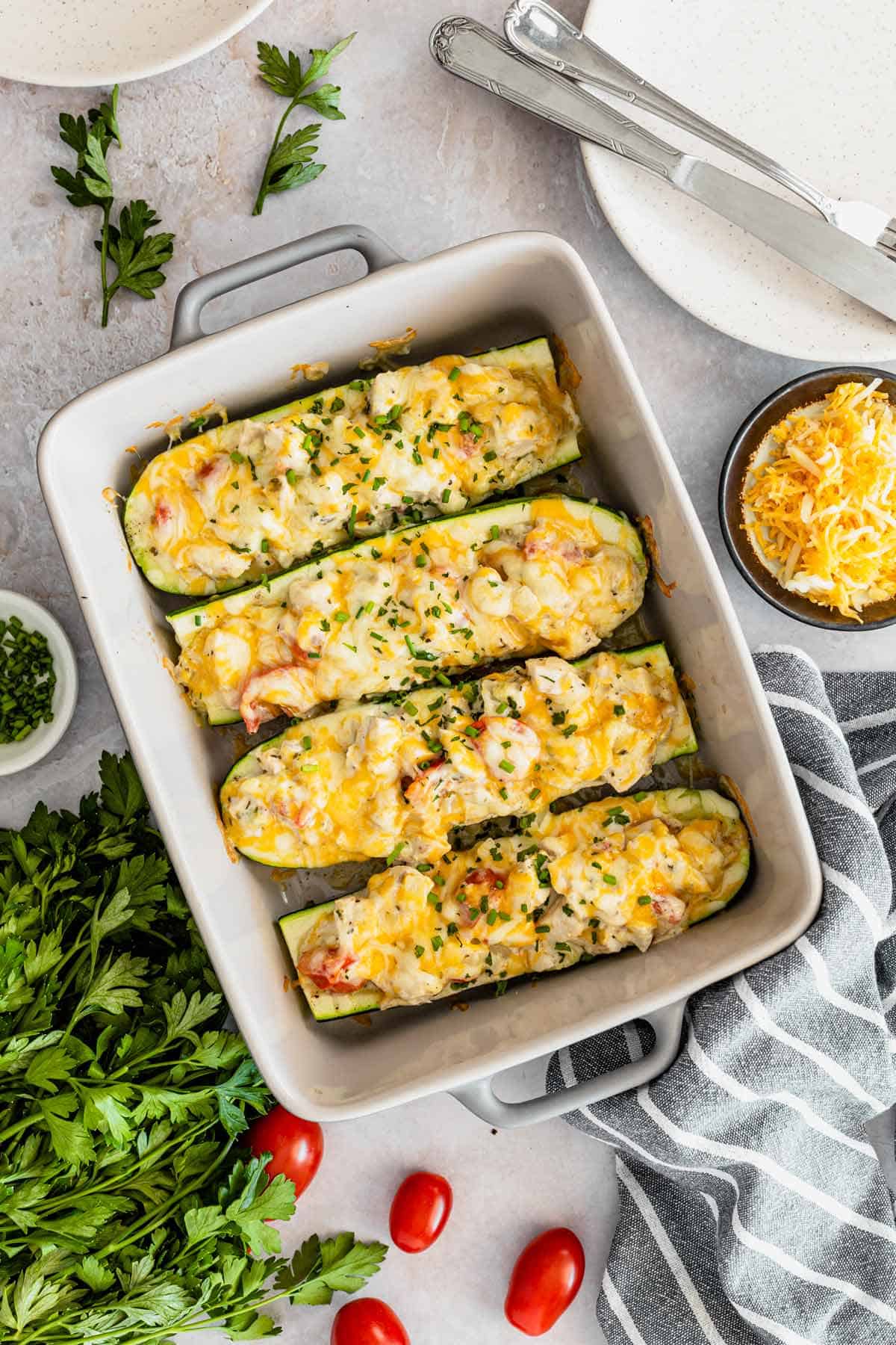 Stuffed zucchini boats filled with chicken parmesan and colby jack cheese in a white baking dish.