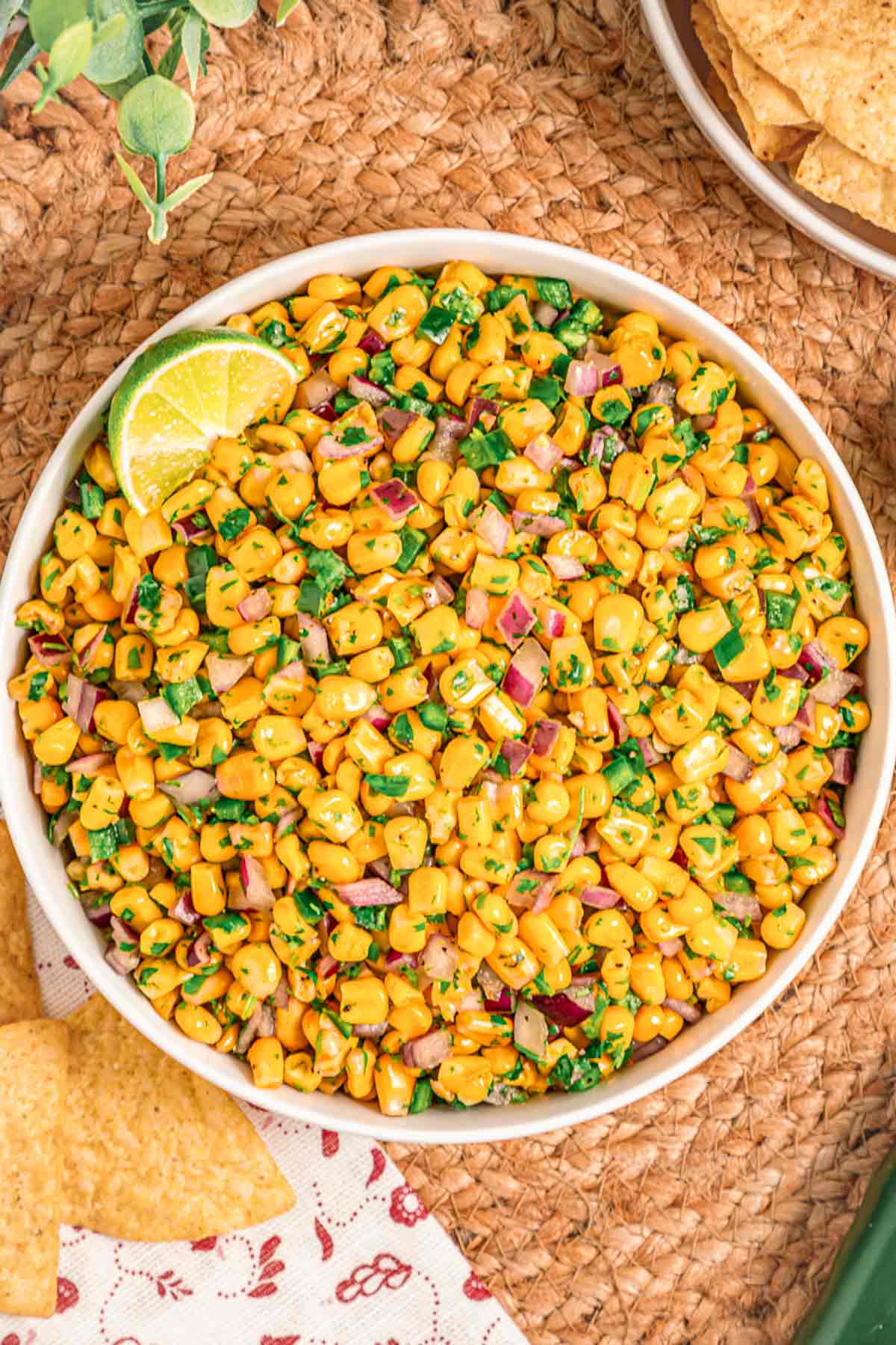 Chipotle-style corn salsa in a bowl with lime wedges and tortilla chips on a neutral background.