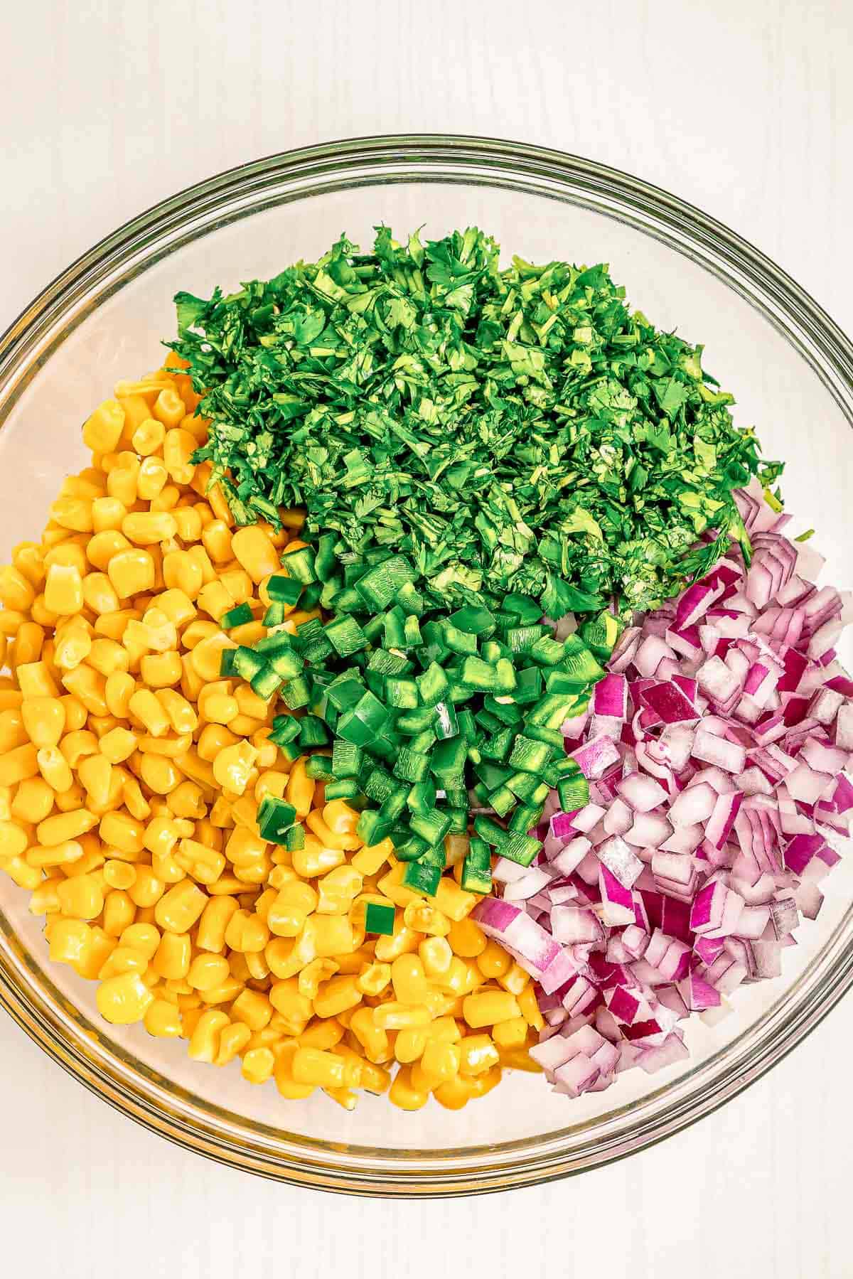 Ingredients for chipotle corn salsa in a bowl with corn, chopped cilantro, and diced red onion, not mixed yet.