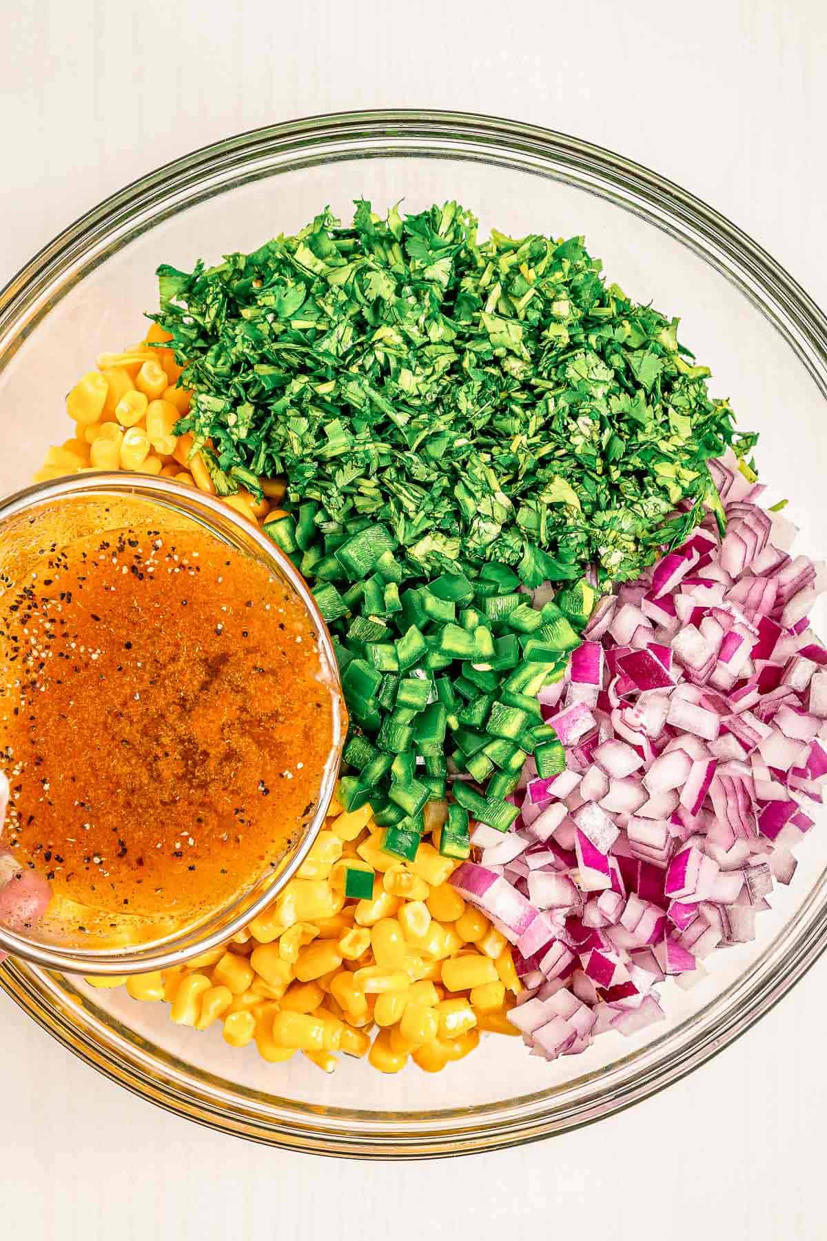 Lime dressing being poured over corn salsa ingredients in a glass bowl before mixing.