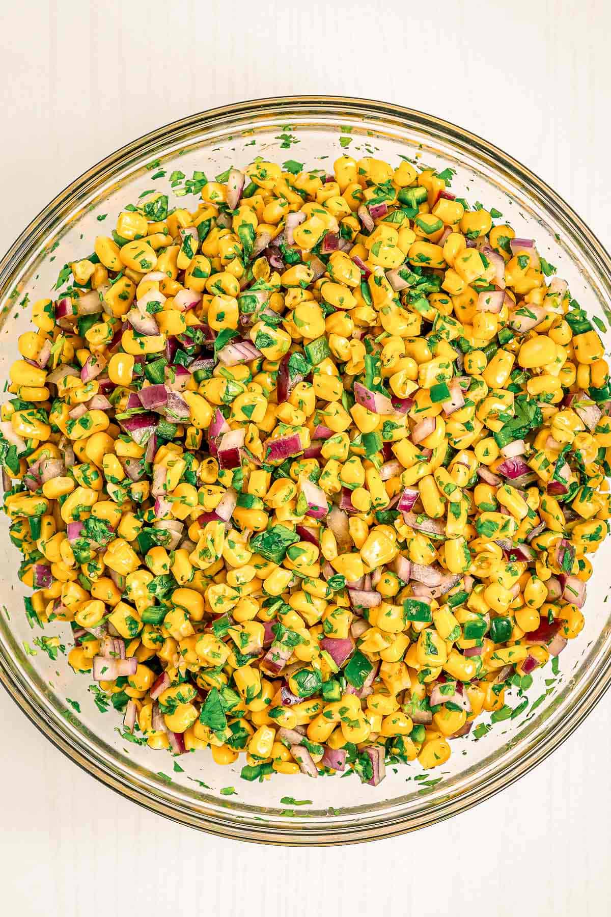 Overhead view of fresh chipotle corn salsa mixed with cilantro, red onion, and jalapeños in a glass bowl.
