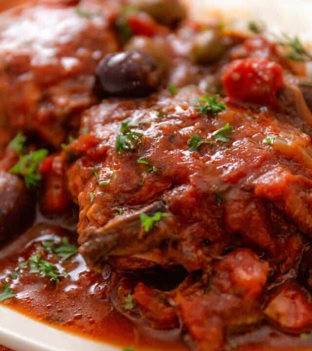 a close up shot of slow cooker chicken thighs in tomato sauce and Italian seasonings and olives (Chicken Cacciatore)