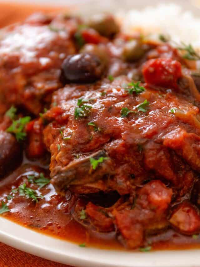 a close up shot of slow cooker chicken thighs in tomato sauce and Italian seasonings and olives (Chicken Cacciatore)