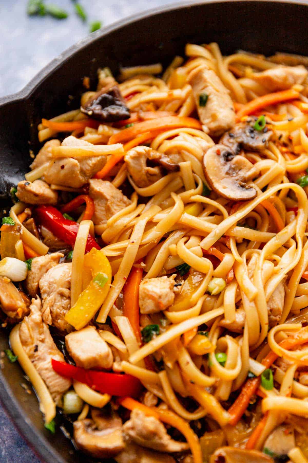 lo mein style noodles with veggies and chicken in skillet.