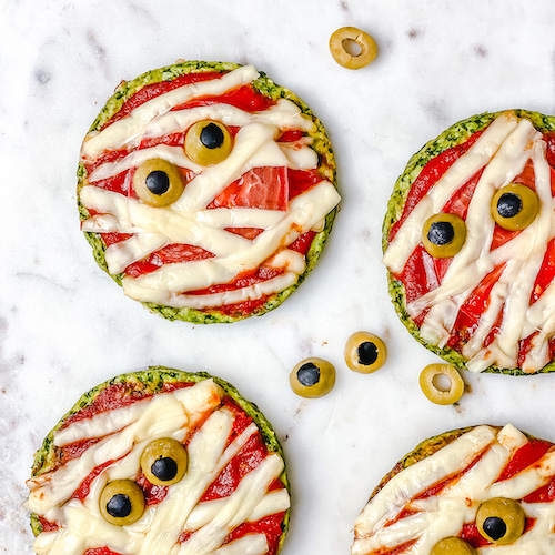 Halloween Mummy Pizzas - is the perfect Halloween party or dinner idea. Make these mummies with your kids for an easy and super flavorful Halloween themed meal. These mini pizzas are also gluten-free! The Yummy Bowl #savouryhalloweenfood #halloweenfoodrecipes #halloweenmummypizza #mummypizza #creepyhalloweenfoodideas #traditionalhalloweenfood #halloweentreats