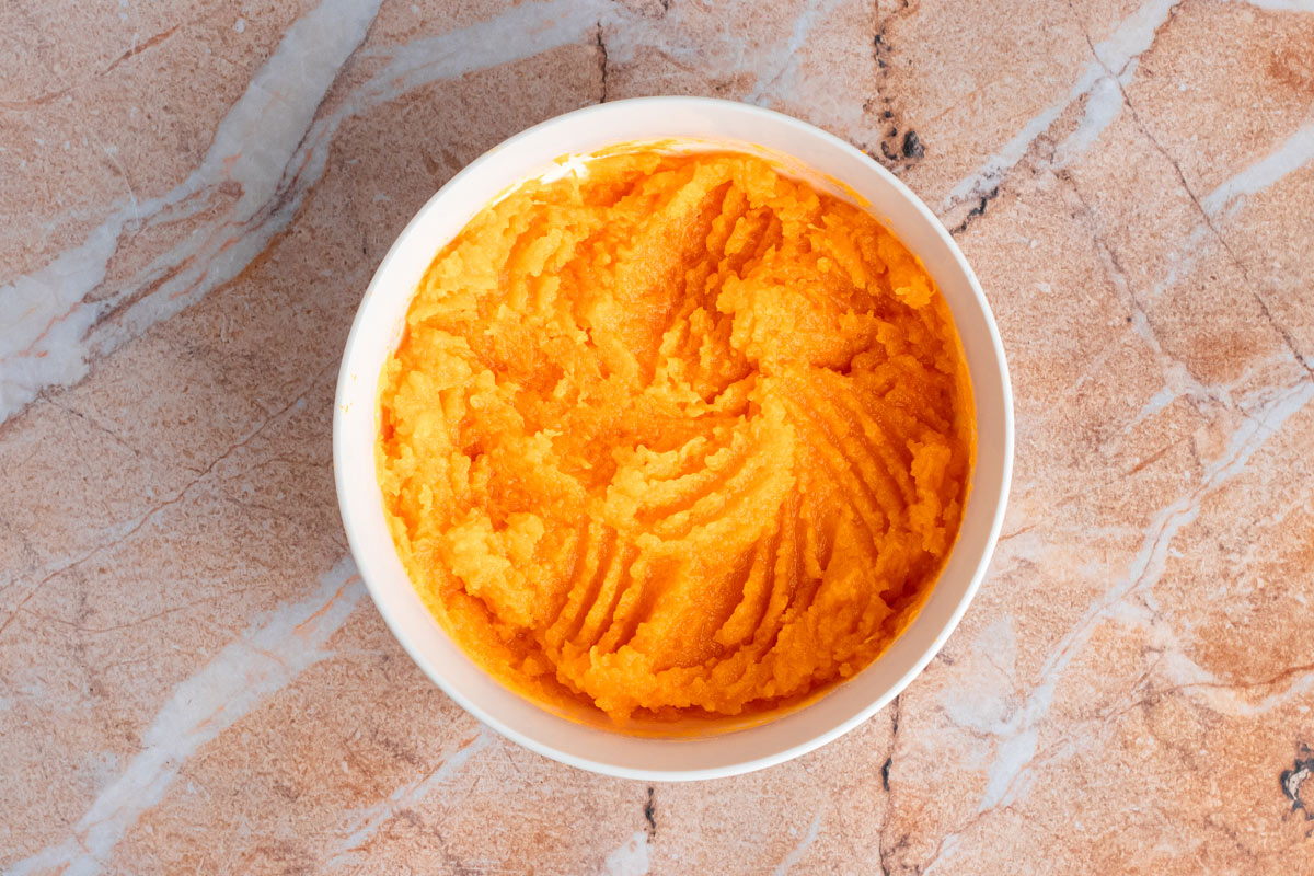 White bowl of smooth canned pumpkin puree on a marble countertop.
