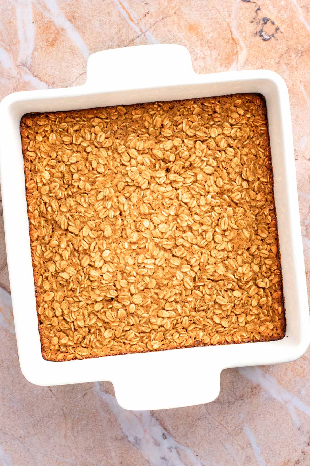 Freshly baked pumpkin baked oatmeal with a golden oat top in a white square baking dish, before cutting or glazing.