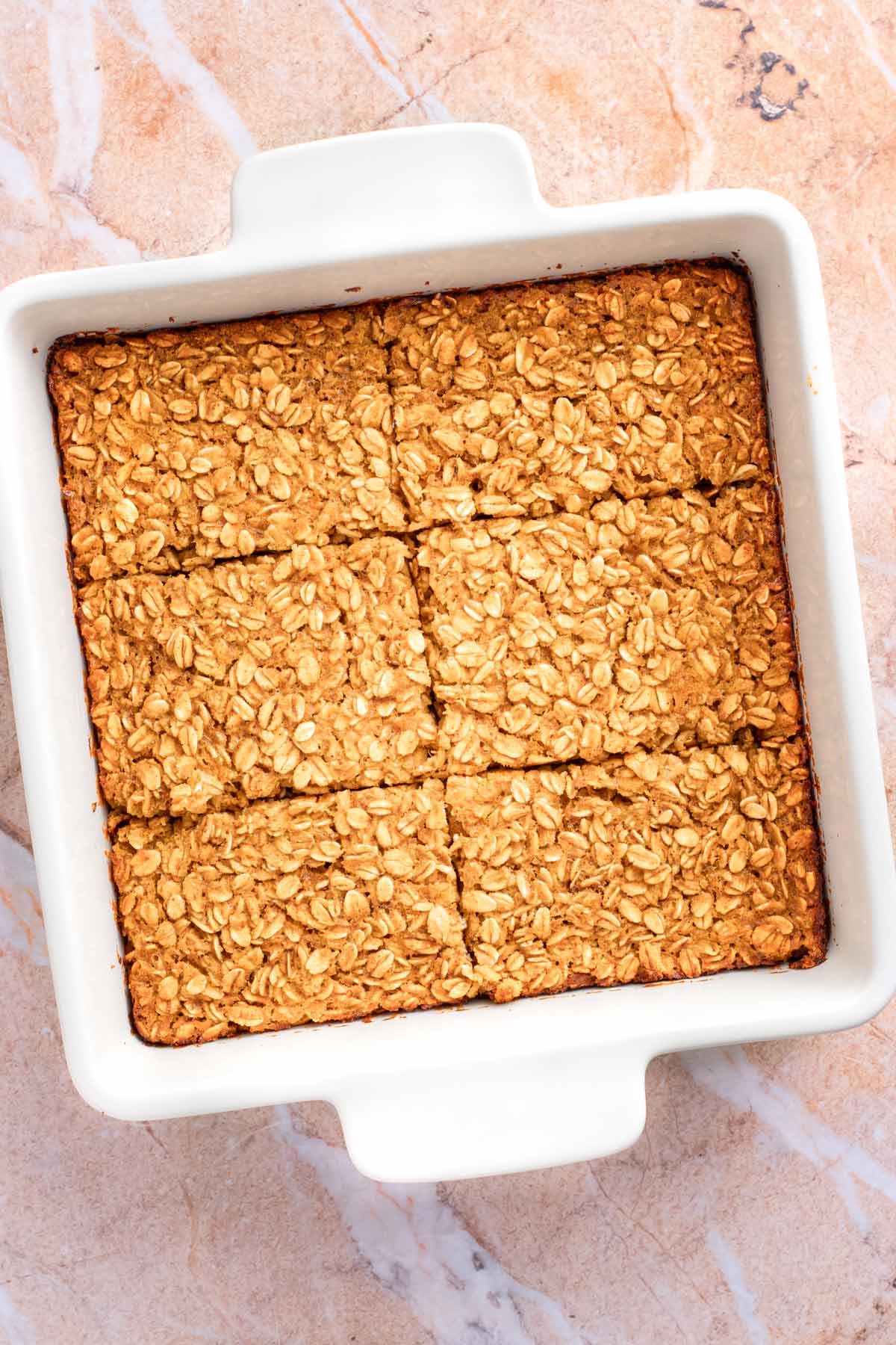 Baked pumpkin oatmeal cut into six squares in a white baking dish, before adding the glaze.