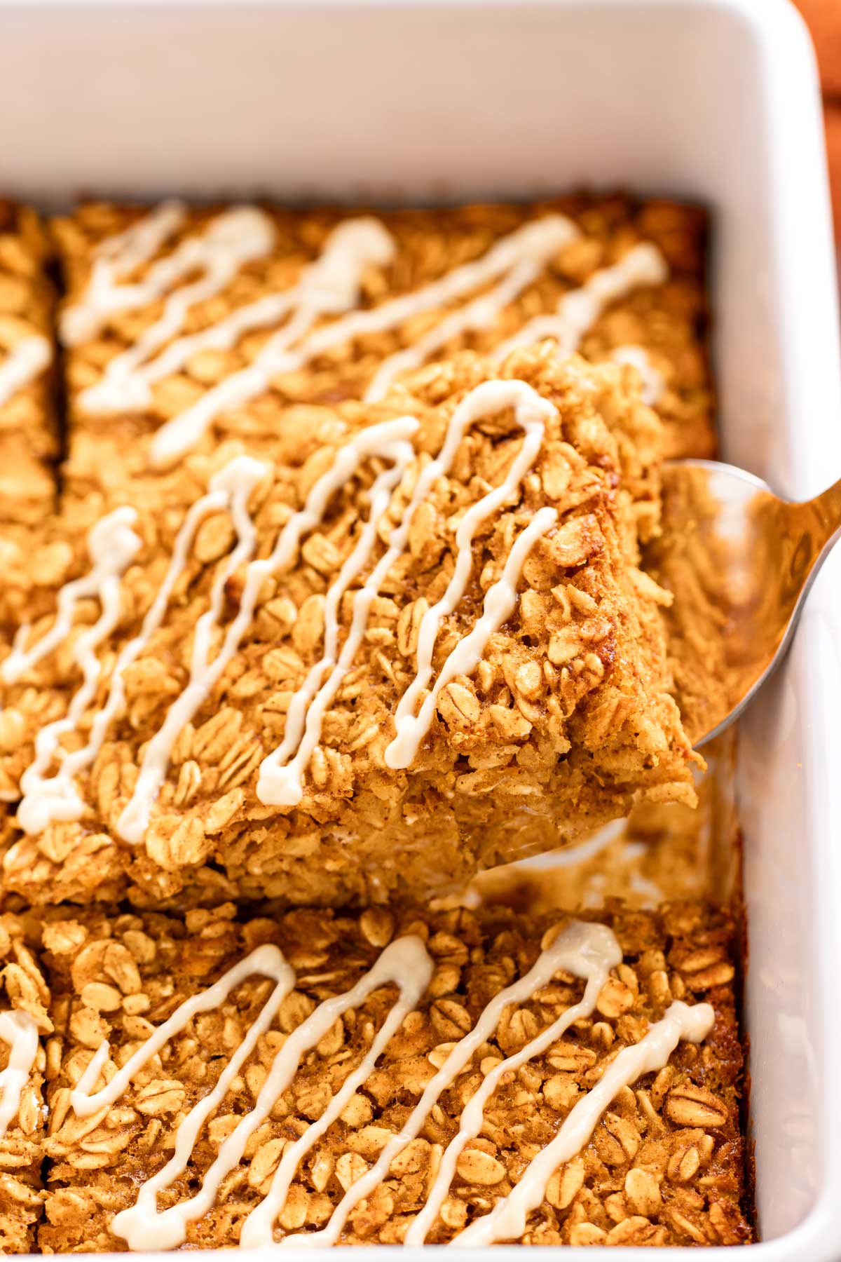 Spatula lifting a glazed square of pumpkin baked oatmeal out of the baking dish, showing the soft, oat-studded inside.