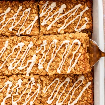 Close up of glazed pumpkin baked oatmeal squares with a spatula lifting one out of the white baking dish.