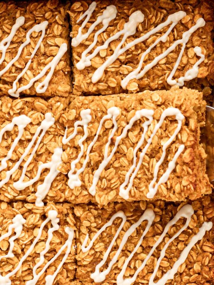 Close up of glazed pumpkin baked oatmeal squares with a spatula lifting one out of the white baking dish.