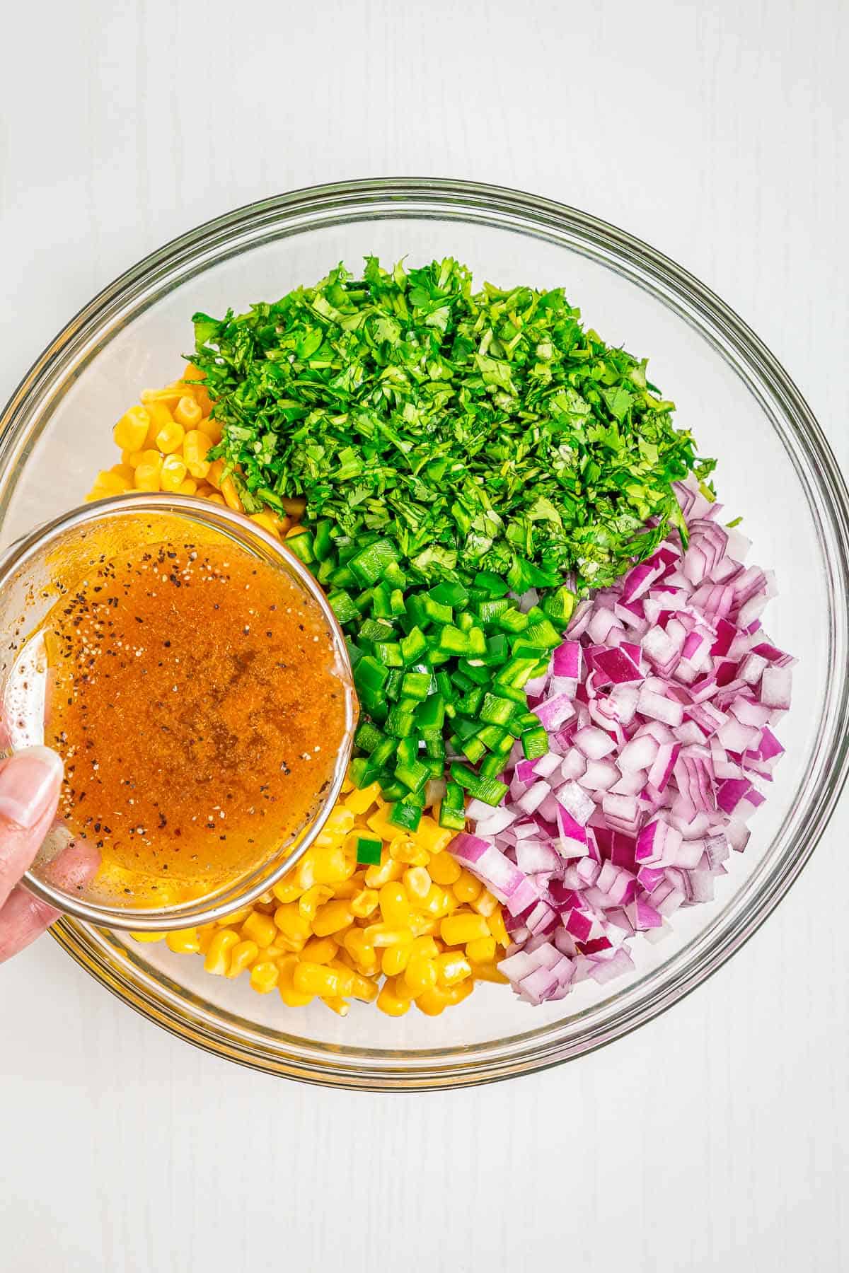 Lime dressing being poured over corn salsa ingredients in a glass bowl before mixing.