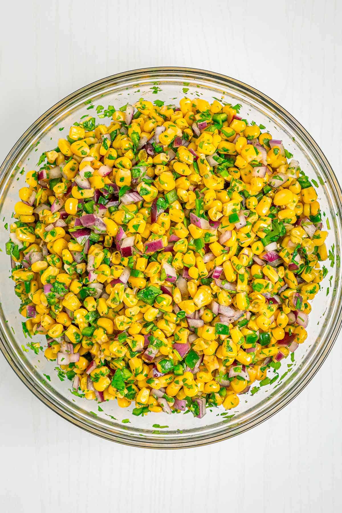 Overhead view of fresh chipotle corn salsa mixed with cilantro, red onion, and jalapeños in a glass bowl.