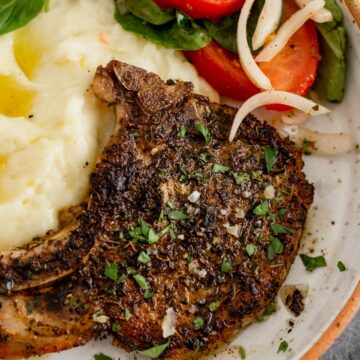 Pan Seared Pork Chop in a plate with mashed potatoes and tomato onion lettuce salad